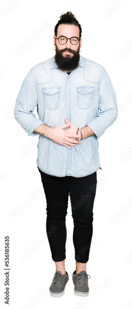 Young hipster man with long hair and beard wearing glasses with hand on stomach because indigestion, painful illness feeling unwell. Ache concept. Young hipster man with long hair and beard wearing glasses with hand on stomach because indigestion, painful illness feeling unwell. Ache concept.