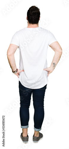 Young hipster man with long hair and beard wearing casual white t-shirt standing backwards looking away with arms on body