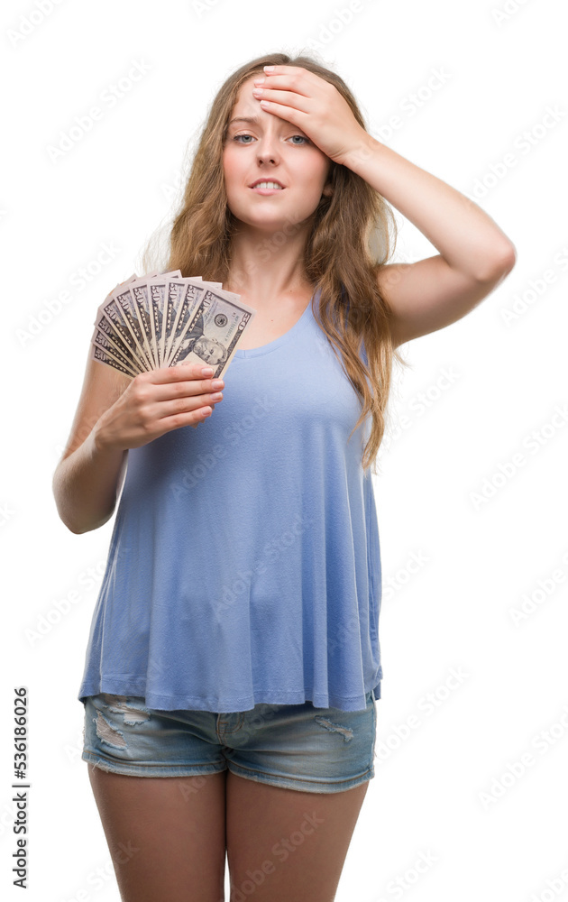 Young blonde woman holding dollars stressed with hand on head, shocked with shame and surprise face, angry and frustrated. Fear and upset for mistake. Young blonde woman holding dollars stressed with hand on head, shocked with shame and surprise face, angry and frustrated. Fear and upset for mistake.