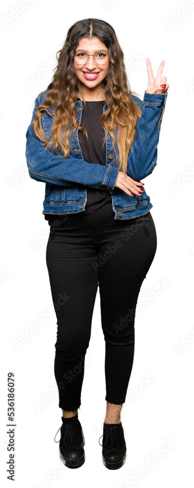 Obraz premium Young beautiful woman wearing glasses and denim jacket smiling with happy face winking at the camera doing victory sign. Number two.