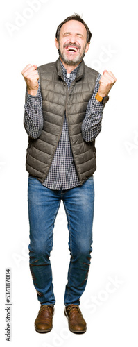 Middle age handsome man wearing winter vest celebrating surprised and amazed for success with arms raised and open eyes. Winner concept. © Krakenimages.com
