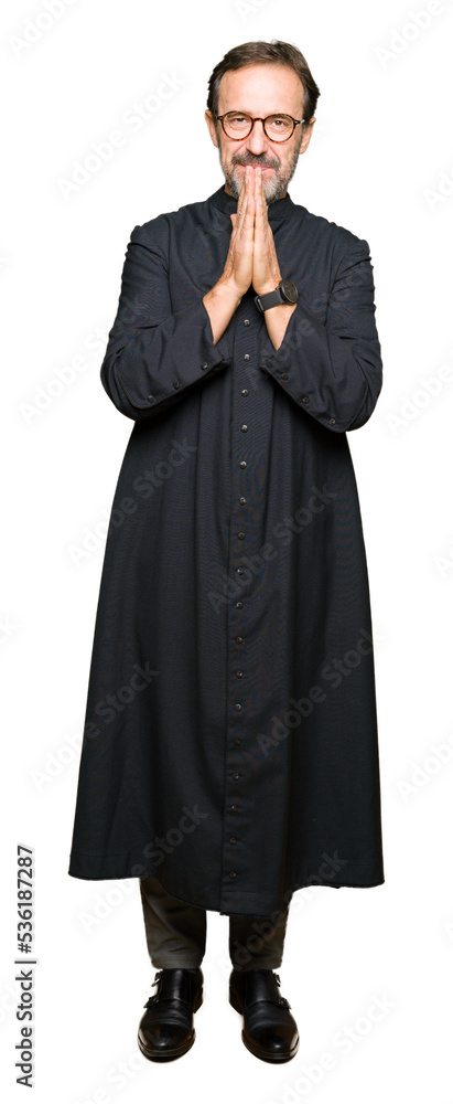 Middle age priest man wearing catholic robe praying with hands together asking for forgiveness smiling confident. Middle age priest man wearing catholic robe praying with hands together asking for forgiveness smiling confident.