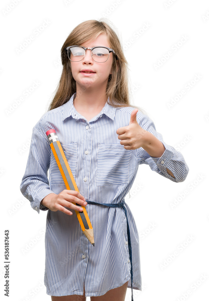 Young blonde child holding big pencil happy with big smile doing ok sign, thumb up with fingers, excellent sign Young blonde child holding big pencil happy with big smile doing ok sign, thumb up with fingers, excellent sign