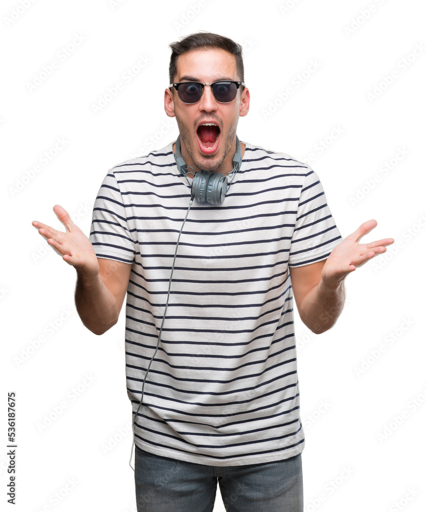 Handsome young man wearing headphones celebrating crazy and amazed for success with arms raised and open eyes screaming excited. Winner concept Handsome young man wearing headphones celebrating crazy and amazed for success with arms raised and open eyes screaming excited. Winner concept