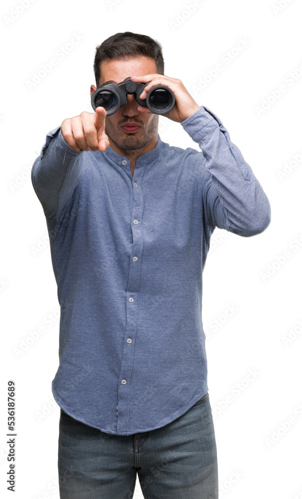 Handsome young man looking through binoculars pointing with finger to the camera and to you, hand sign, positive and confident gesture from the front Handsome young man looking through binoculars pointing with finger to the camera and to you, hand sign, positive and confident gesture from the front