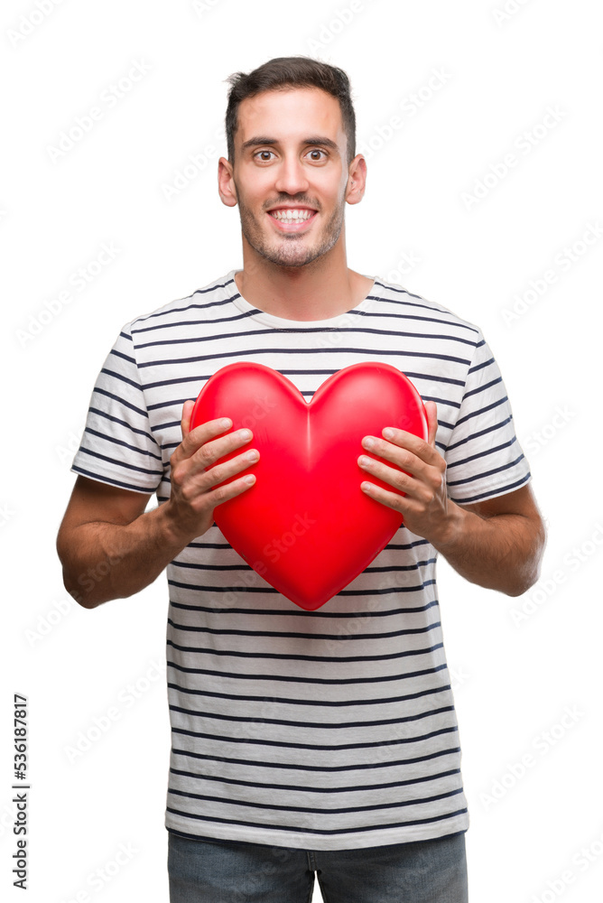 Handsome young man in love holding red heart with a happy face standing and smiling with a confident smile showing teeth Handsome young man in love holding red heart with a happy face standing and smiling with a confident smile showing teeth