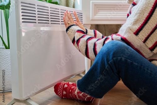 Close-up of woman hands legs warming near electric heating radiator