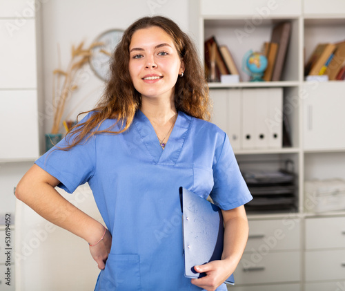 Young smiling female nurse holding folder in hands in modern medical office