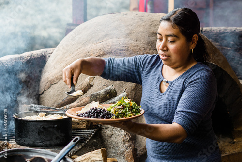 Portrait of a Latin woman in a rural community cooking beans, rice and salad, with a stone oven in Chiapas Mexico. Copy space.