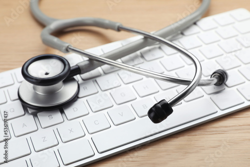 Computer keyboard with stethoscope on wooden table, closeup