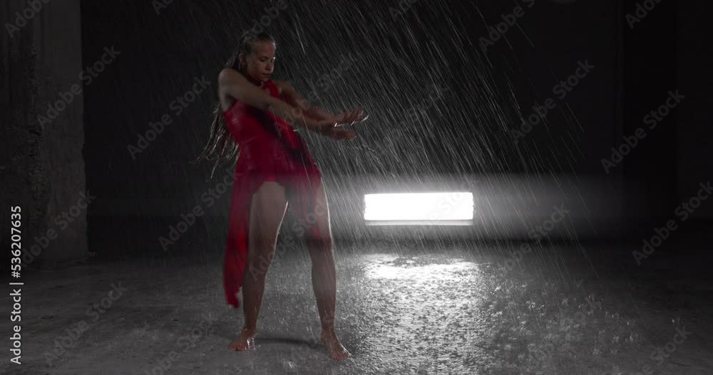 Tempting Young Woman Dancer in Red Dress Performing in the Rain in Dark Studio Tempting Young Woman Dancer in Red Dress Performing in the Rain in Dark Studio