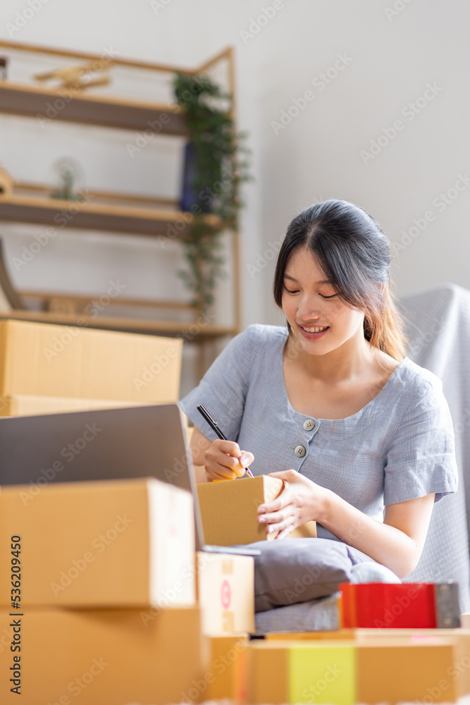Young Asian woman small business owner SME online marketing at home. confirm orders from customers preparing package product with box and laptop, SME entrepreneur or freelance life style concept.