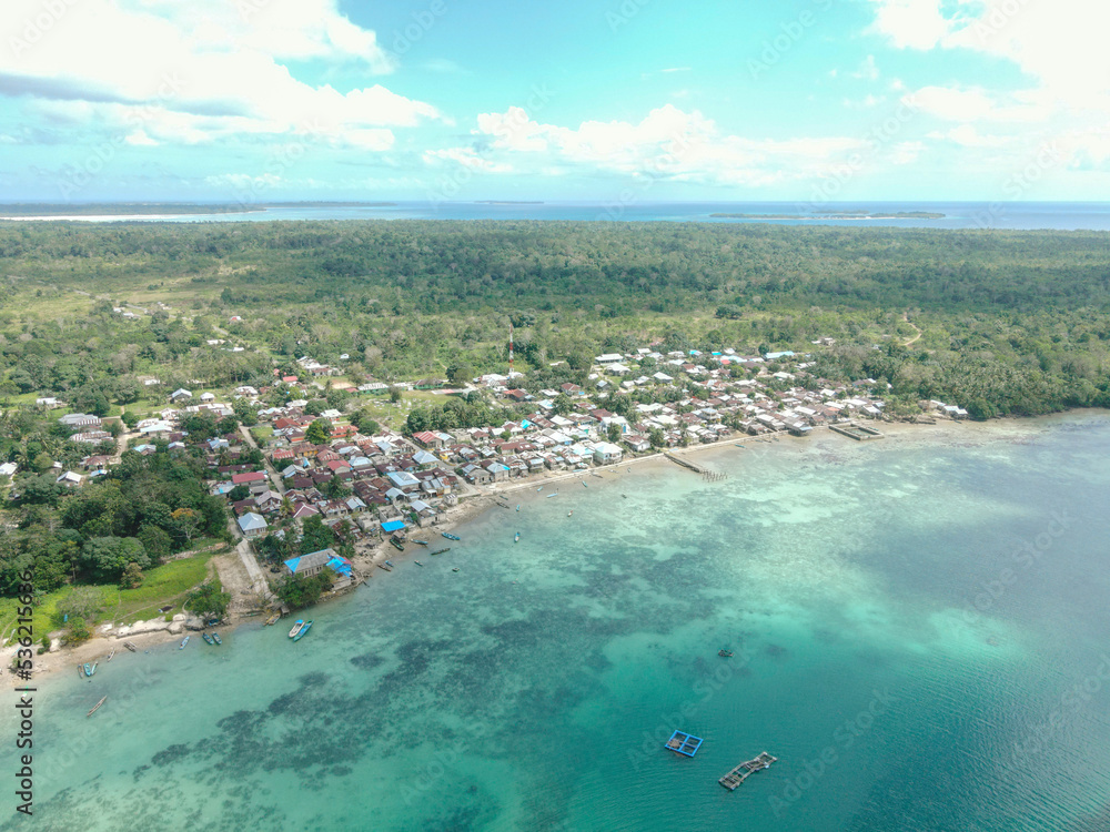 Aerial view of village near beautiful beach with small island in the background in Maluku, Indonesia