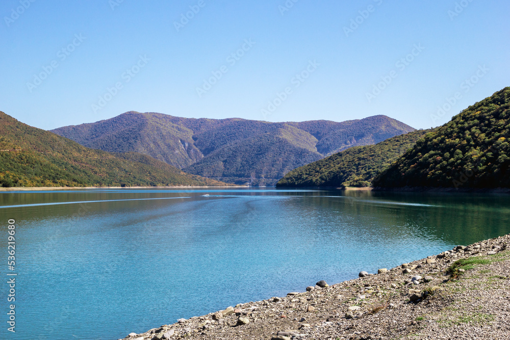 Scenic view on bank of lake with blue water and mountains in sunny weather. Caucasus Mountains, Georgia.