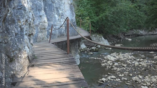 Wooden footbridge on stone wall over mountain creek photo