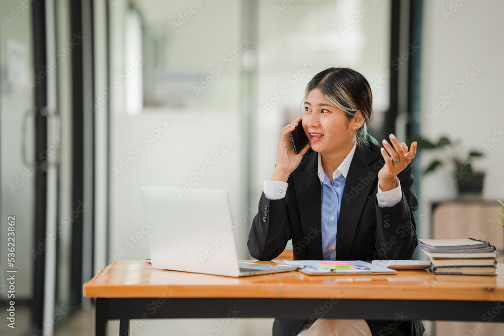 Young accountant working with smartphone and laptop with financial graph documents on table Young accountant working with smartphone and laptop with financial graph documents on table