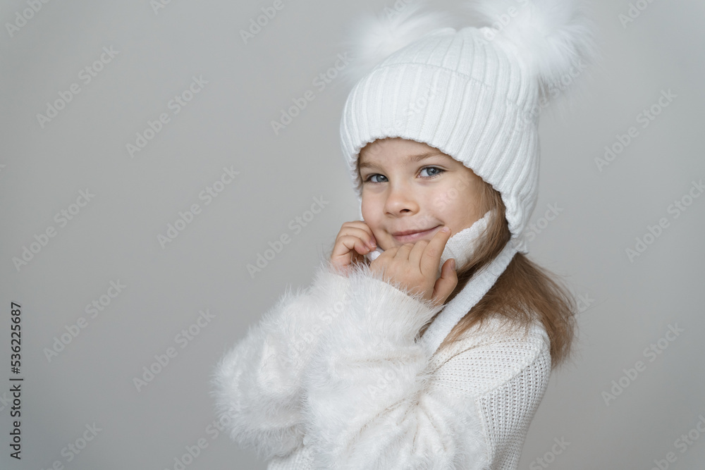 trendy warm winter - beautiful kid girl in white wool winter hat and knitted sweater. Portrait of beauty winter girl in woolen clothing. trendy warm winter - beautiful kid girl in white wool winter hat and knitted sweater. Portrait of beauty winter girl in woolen clothing.