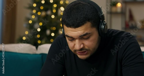 Upset man listening to music in headphones. He is wearing black sweater. Song he was listening to with his ex is playing in headphones. Man sings along in frustration, because he misses the girl. photo