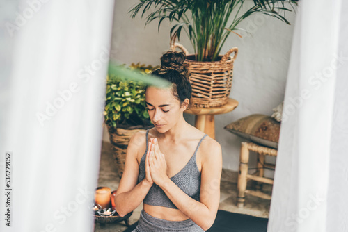 Young woman sitting in the lotus position on floor in a cozy boho room.