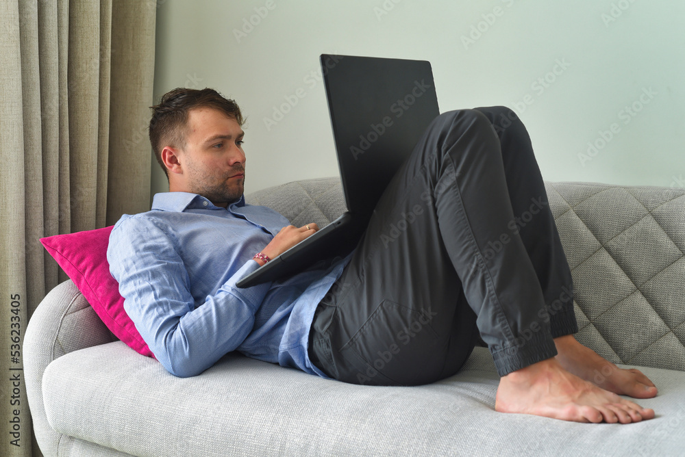 Young man freelancer working from home with his laptop laying on couch