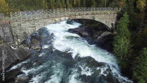 old mossy stone bridge with roaring river stream underneath overview footage photo