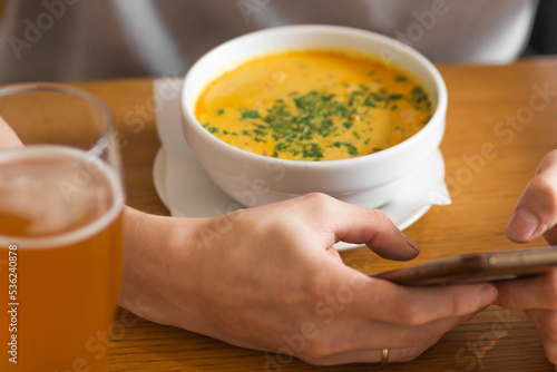 Man's hands holds and using cellphone. Man eating thai curry soup with glass of beer and checking smartphone in cafe.