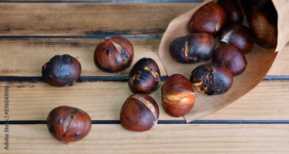 roasted chestnuts in a papaer bag spilled on wooden table roasted chestnuts in a papaer bag spilled on wooden table