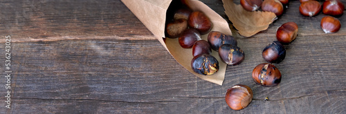 roasted chestnuts  in a papaer bag spilled on wooden table