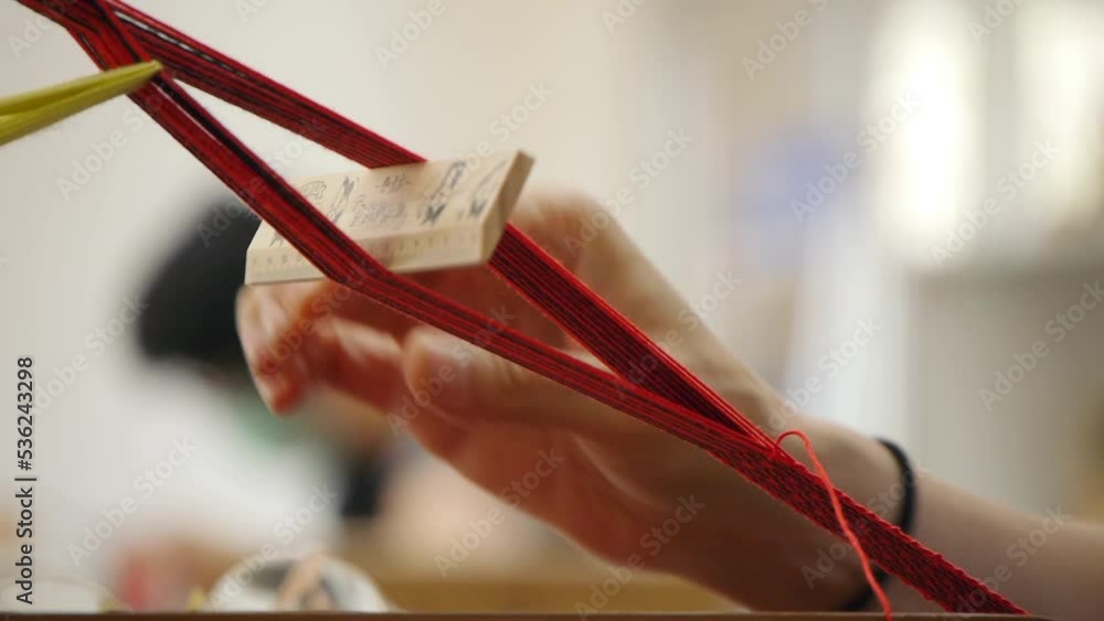 Fingers and hands of person threading yarn and pressing strings on loom