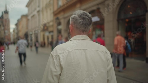 Back view of the man walking in busy Floriańska Street where numerous pedestrian are also walking photo