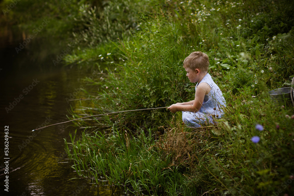 Boy fisherman, catches fish on the river bank in summer Boy fisherman, catches fish on the river bank in summer
