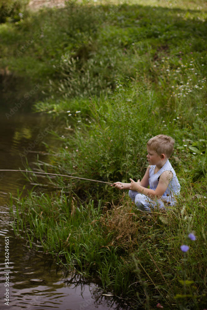 Boy fisherman, catches fish on the river bank in summer