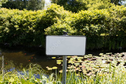 Blank signboard outdoors. Small forest fishing pond. Dangerous river swimming accident. Closeup white metal sign at green background