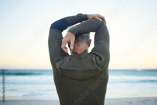 Fitness, surf and man stretching on beach to warm up before training in ocean water. Fitness, freedom and surfer with wellness, health and active lifestyle doing arm exercise for surfing at seaside.