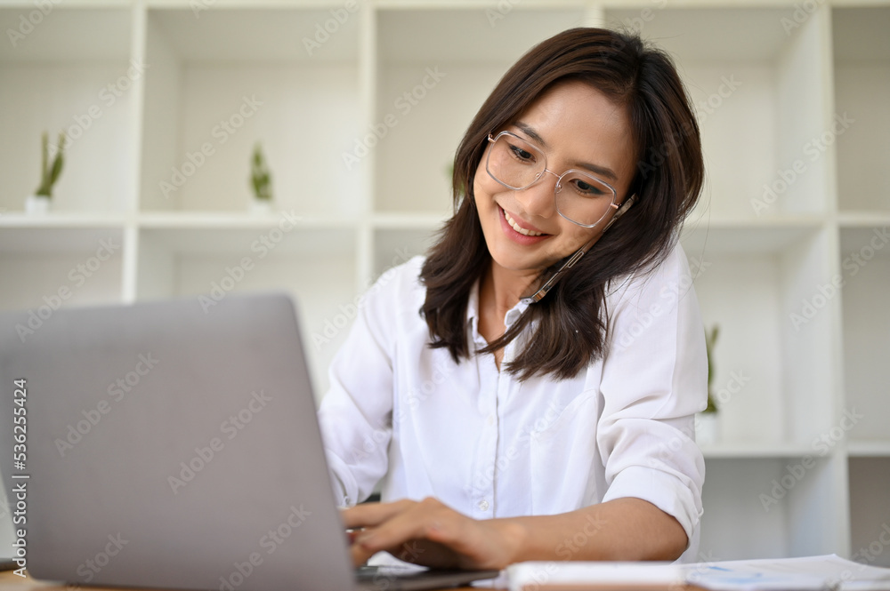 Beautiful Asian female secretary or assistant working, talking on the phone with her client Beautiful Asian female secretary or assistant working, talking on the phone with her client