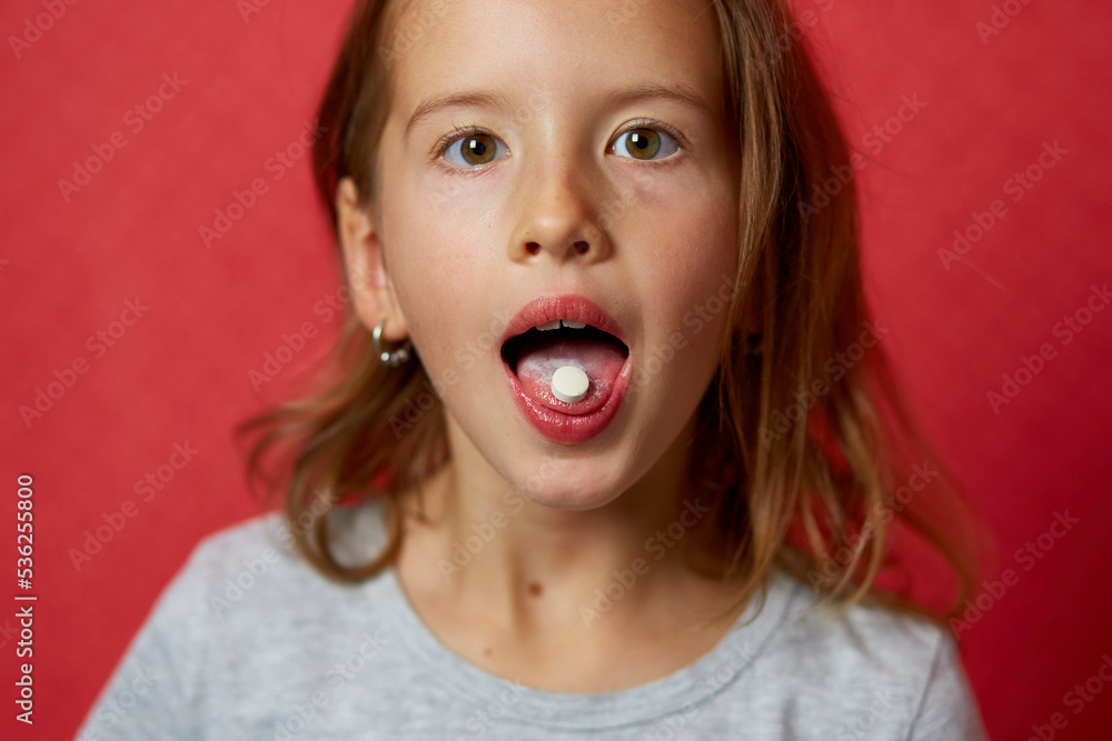 Portrait happy girl take capsule pill on her tongue on red background Portrait happy girl take capsule pill on her tongue on red background