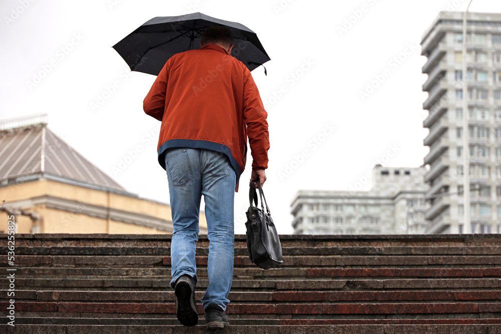 Man with umbrella walking up the steps on city buildings background. Rain in autumn city Man with umbrella walking up the steps on city buildings background. Rain in autumn city