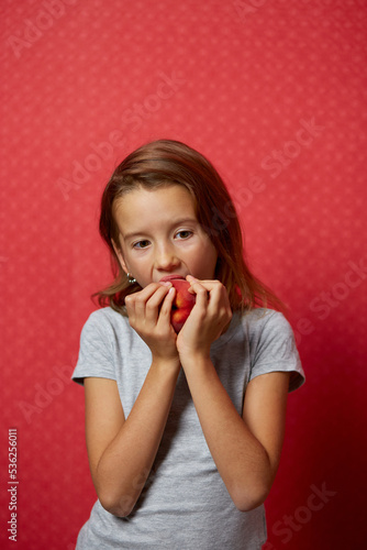 Portrait happy girl eats a peach on a red background