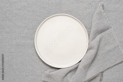 Empty beige plate mockup with gray linen napkin on gray linen background. Top view, flat lay, copy space.