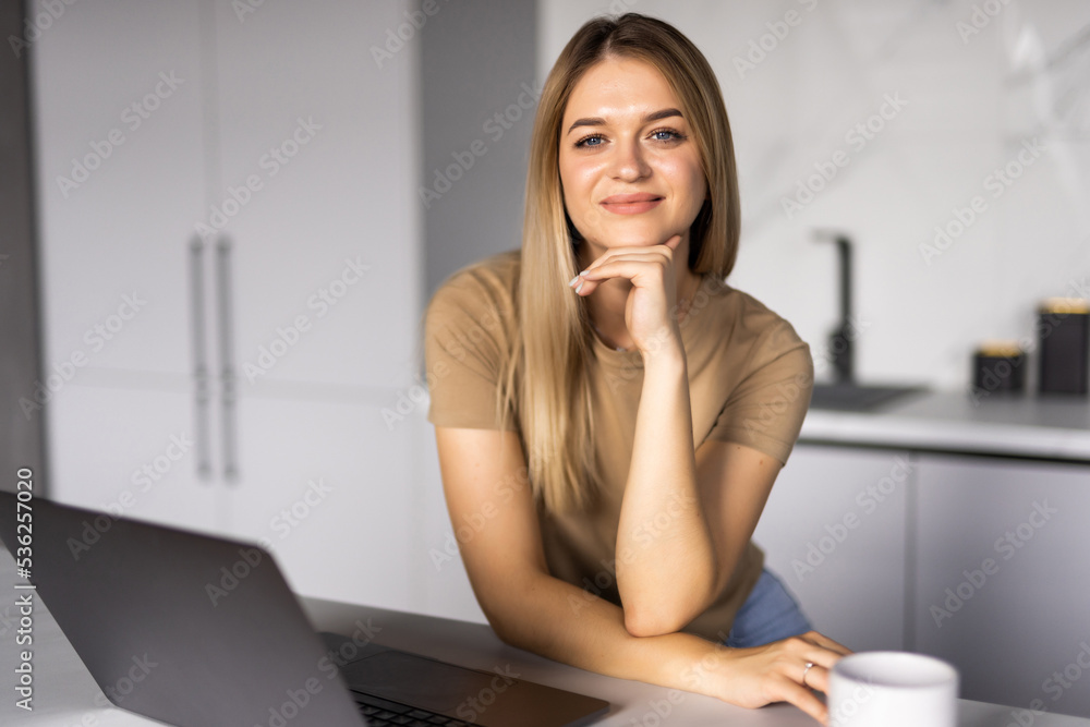 Smiling young woman making video call and heaving a breakfast in her kitchen. Smiling young woman making video call and heaving a breakfast in her kitchen.