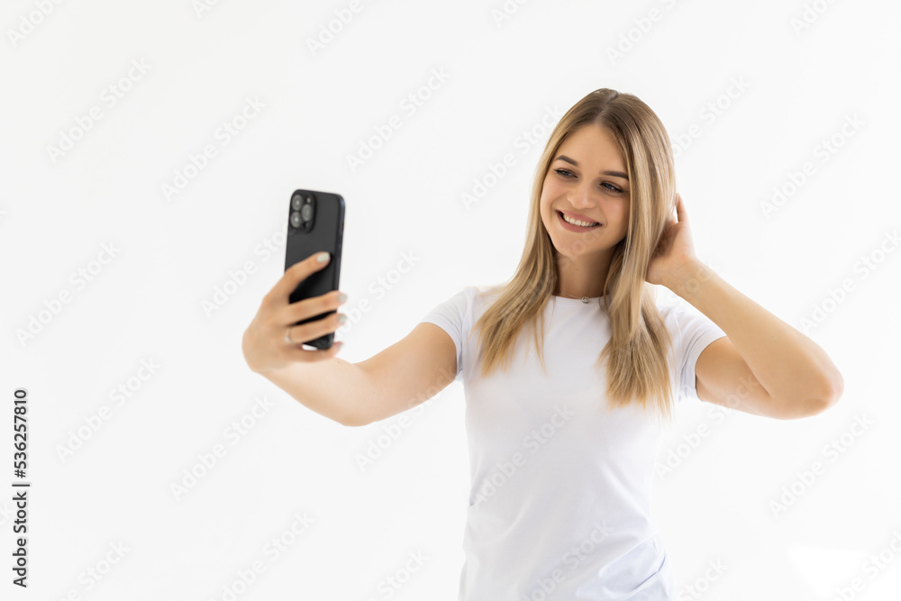 Portrait of a smiling cute woman making selfie photo on smartphone on a white background Portrait of a smiling cute woman making selfie photo on smartphone on a white background