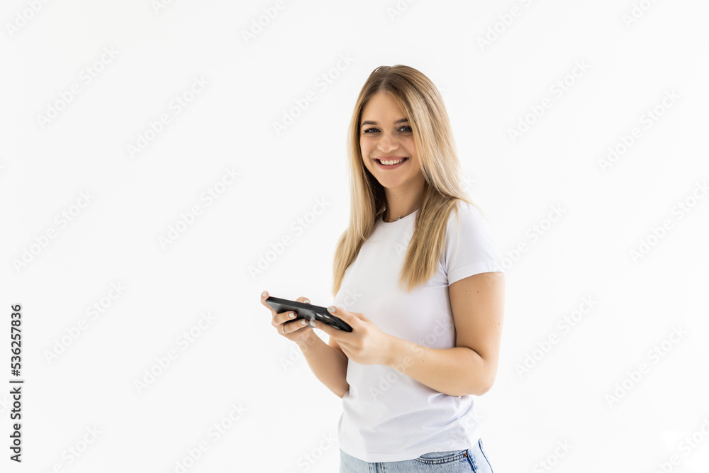 Photo of a shocked surprised young woman posing isolated over white wall background using mobile phone. Photo of a shocked surprised young woman posing isolated over white wall background using mobile phone.