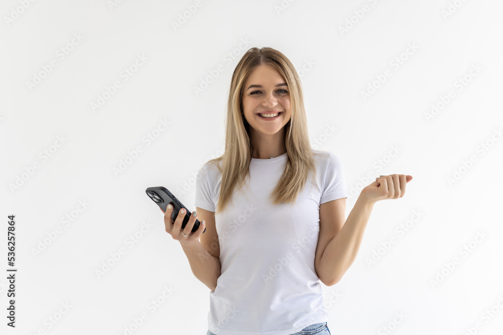 Young woman use smartphone impressed social media like feedback win raise fists scream yes over white grey background Young woman use smartphone impressed social media like feedback win raise fists scream yes over white grey background