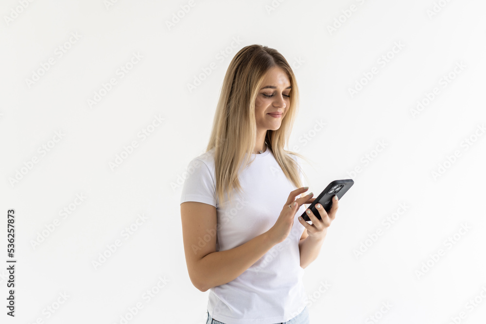 Photo of a shocked surprised young woman posing isolated over white wall background using mobile phone. Photo of a shocked surprised young woman posing isolated over white wall background using mobile phone.