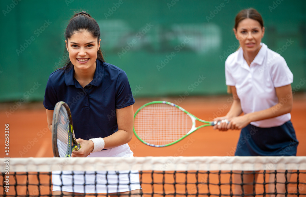Young happy women friends playing tennis at tennis court. People sport concept