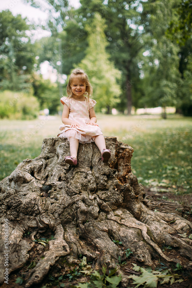 little girl sitting on a tree stump in a park Stock Photo | Adobe Stock