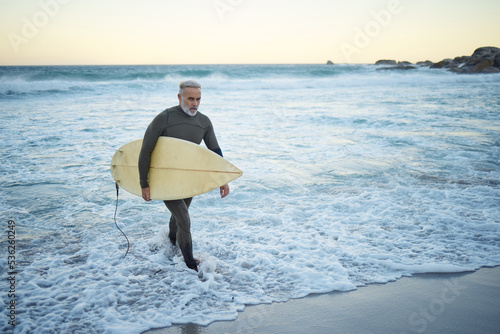 Canvas Print Surfing, surfboard and senior man on beach for water sports while walking on adventure after riding sea waves on a overcast day