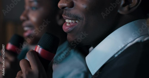 Close-up of boy and girl of African appearance singing karaoke. Young people have beautiful white teeth, hold microphones and sing lyrical song. They are having fun and smiling. photo