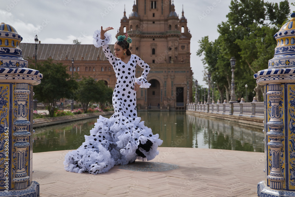 Young teenage woman in white dance suit with black polka dots and green carnations in her hair, dancing flamenco by a lake. Flamenco concept, dance, art, typical Spanish dance. - obrazy, fototapety, plakaty 