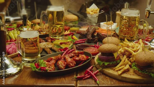 Table served with beer fast food fried fries chicken wings burgers  Austrian sausages various types of sauces . Camera moving across food Shot on ARRI ALEXA Cinema Camera with Laowa lens . Slow motion photo